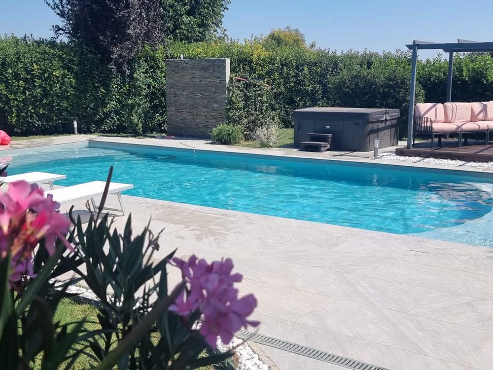 Piscina realizzata in giardino, con bordo in pietra chiara, oleandri in fiore e pergola